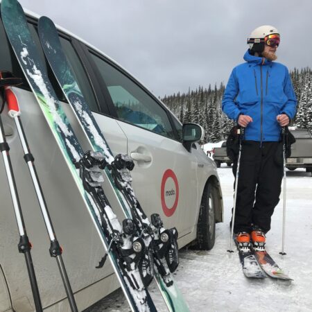 A skier leaning skis against a MODO car in Vancouver.
