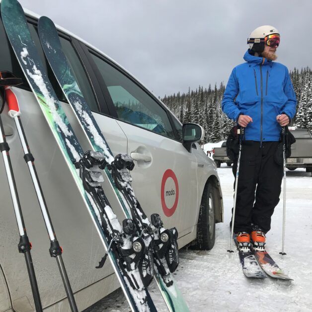 A skier leaning skis against a MODO car in Vancouver.
